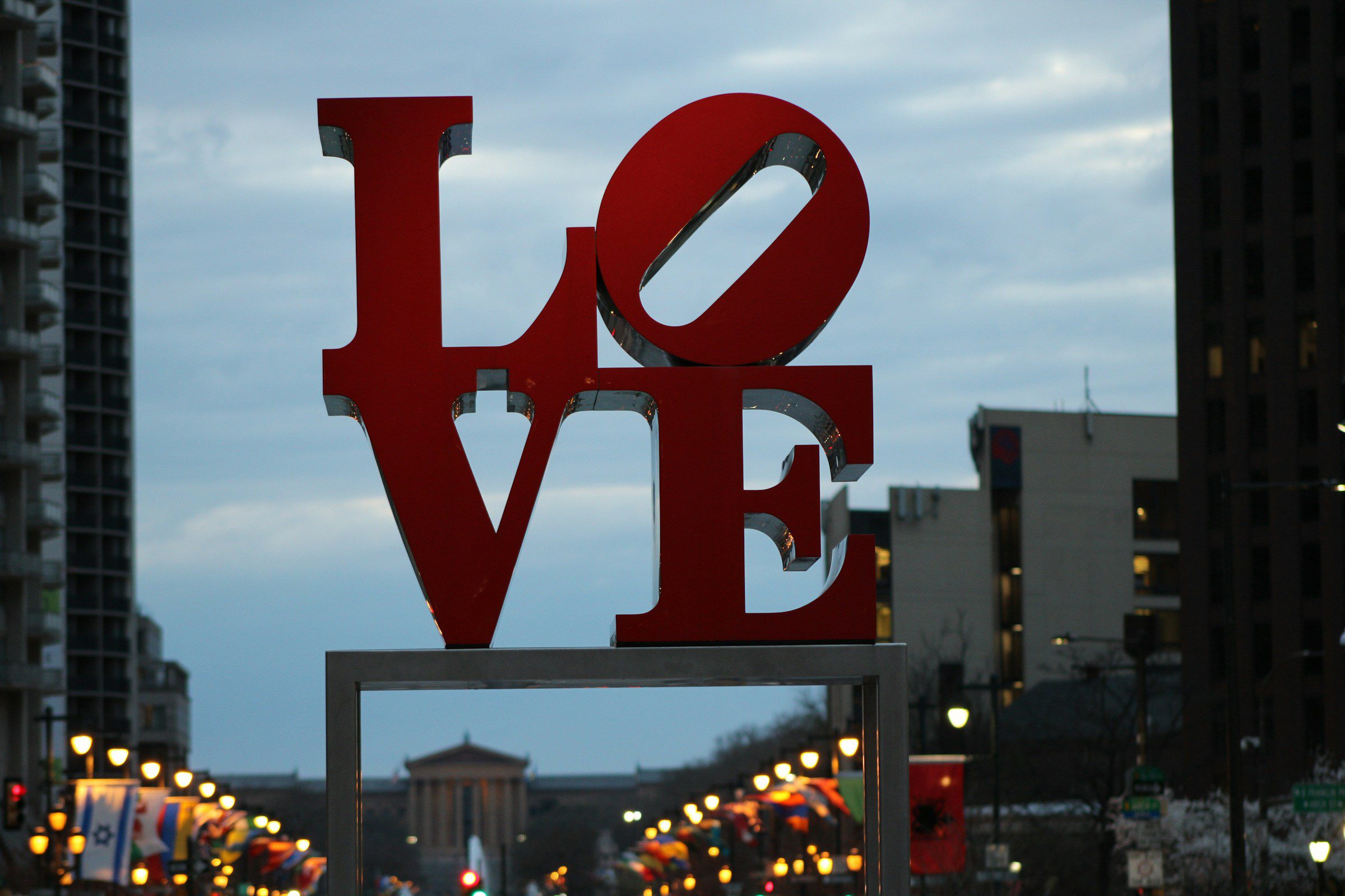 LOVE art sign in Philadelphia's Love Park / JFK Plaza at dusk with streetlights and buildings visible in background.